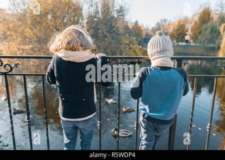 Kinder, Junge und Mädchen stehend mit dem Rücken in der Nähe von Teich im Park, auf der Enten, sonnigen Herbst Tag im Park suchen, goldenen Stunde. Stockfoto