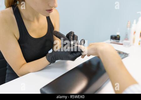 Nahaufnahme der professionelle Maniküre. Nagelstudio frau Hände in schwarz Handschuhe, Maniküre mit Hilfe professioneller Tools. Nagel- und Handpflege in beaut Stockfoto