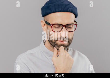 Headshot von traurig einsam schweren männlichen hält Hand unter das Kinn, hat dunkle Borsten, schaut, denkt über Förderung und starten neue Karriere, trägt spectac Stockfoto