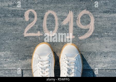 Weibliche Füße mit Text 2019 auf Asphalt geschrieben. Stockfoto