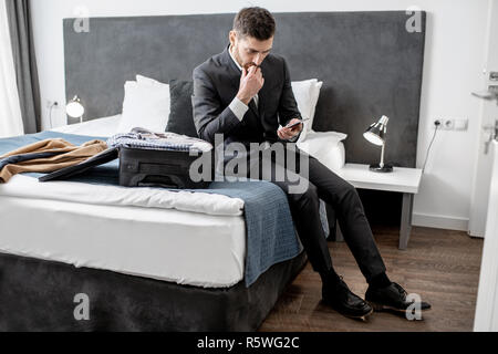 Porträt einer stattlichen Geschäftsmann auf dem Bett zu sitzen mit Gepäck in das Zimmer während der Geschäftsreise Stockfoto