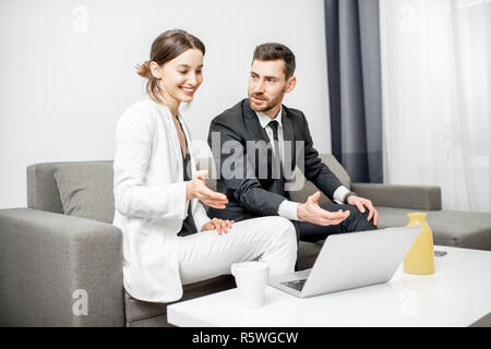 Elegante Mann und Frau gekleidet in die Anzüge Geschäft zusammen sitzen auf der Couch mit dem Laptop zu Hause oder im Büro Stockfoto