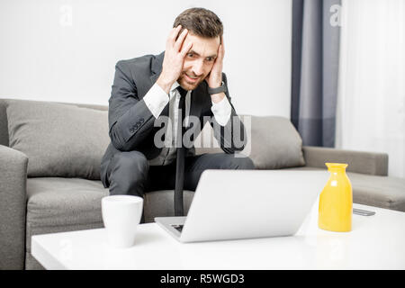 Portrait von ein Geschäftsmann mit Emotionen verwirrt und verzweifelt seinen Kopf sitzen auf der Couch mit dem Laptop Holding Stockfoto