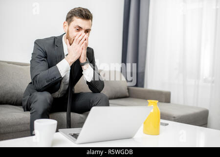 Portrait von ein Geschäftsmann mit Emotionen verwirrt und verzweifelt seinen Kopf sitzen auf der Couch mit dem Laptop Holding Stockfoto