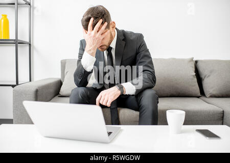 Portrait von ein Geschäftsmann mit Emotionen verwirrt und verzweifelt seinen Kopf sitzen auf der Couch mit dem Laptop Holding Stockfoto