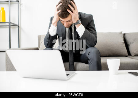 Portrait von ein Geschäftsmann mit Emotionen verwirrt und verzweifelt seinen Kopf sitzen auf der Couch mit dem Laptop Holding Stockfoto