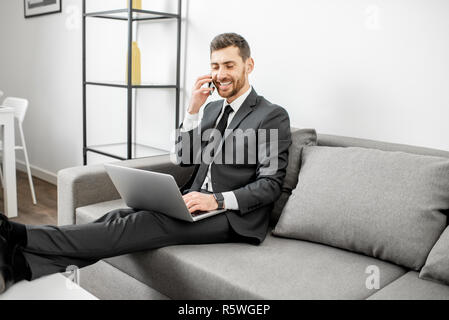 Elegante Geschäftsmann im Anzug arbeiten mit Laptop und Telefon auf die Couch zu Hause oder Büro bequem gekleidet Stockfoto