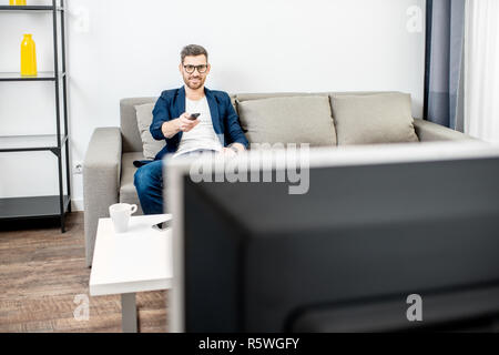 Gut aussehender Geschäftsmann gekleidet beiläufig Fernsehen auf der Couch zu Hause Stockfoto