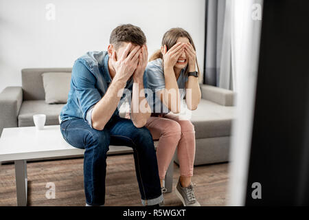 Junges Paar mit Angst Emotionen Fernsehen sitzen zusammen auf dem Tisch zu Hause Stockfoto