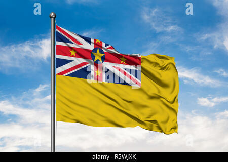 Flagge von Niue winken im Wind gegen Weiße bewölkt blauer Himmel. Stockfoto