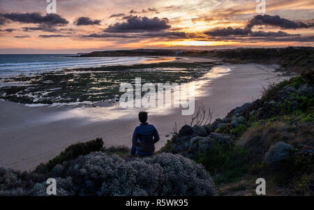 Eine Frau in den späten 20s beobachtet den Sonnenuntergang am Strand zurück, Torquay in Australien Stockfoto