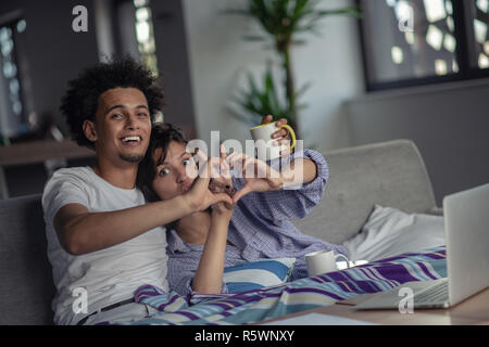 Junge attraktive diverse Paar damit im Internet surfen, können Sie über einen Laptop-Computer, ein Lächeln auf den Lippen. Stockfoto
