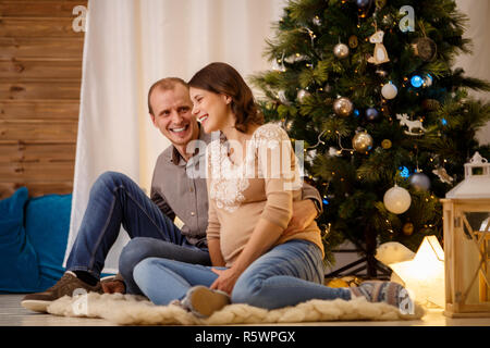 Foto von jungen schwangeren Paar auf dem Hintergrund von geschmückten Tannenbaum Stockfoto