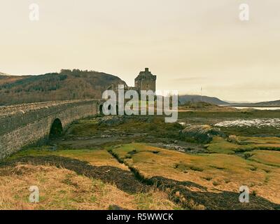 Gezeiten der See am Eilean Donan Castle, Schottland. Die beliebten steinerne Brücke über die Reste von Wasser mit massiven Büschel von Wasser Algen. Schwaches Licht Stockfoto