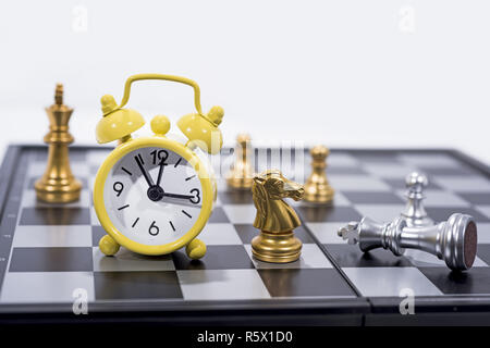 Schachbrett isoliert auf weißem Hintergrund. Die goldenen und silbernen Figuren mit kleinen gelben Wecker. Stockfoto
