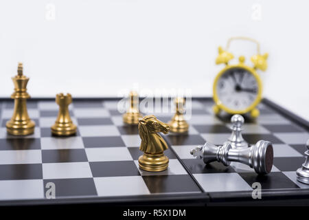 Schachbrett isoliert auf weißem Hintergrund. Die goldenen und silbernen Figuren mit kleinen gelben Wecker. Stockfoto