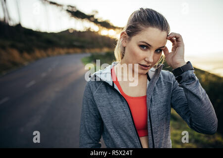 Portrait einer weiblichen Athleten stehen auf der Straße, während Ihr Morgen fitness training. Frau in fitness Verschleiß zu Fuß auf eine leere Straße in den Morgen. Stockfoto