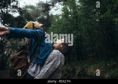 Mann, der seine Frau, die mit ausgestreckten Armen und fangen Regentropfen auf der Zunge. Romantisches Paar genießen den Regen. Stockfoto