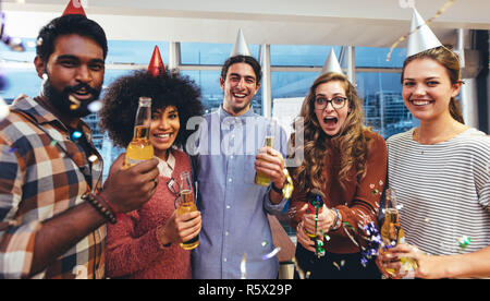 Lächelnde Männer und Frauen in der Partei Kappen und Holding Bier genießen eine Party. Mitarbeiter Spaß an einer Partei im Büro Erfolg zu feiern. Stockfoto