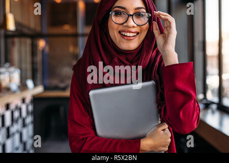 Schönen muslimischen Frau mit Laptop in der Hand einstellen ihre Brille im Coffee Shop. Weibliche im hijab im Coffee Shop. Stockfoto