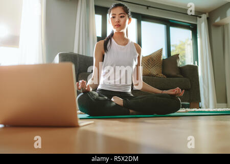 Schöne chinesische Frau trainieren Yoga während sie Lernvideos auf dem Laptop. Passende Frau beobachten Tutorial auf Laptop zu Hause, und Yoga werden Stockfoto