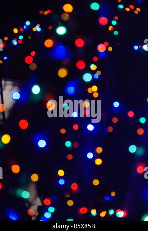 Rot, Grün, Blau, Weiß, Grün, Lila und orange Bokeh auf einem blauen/schwarzen Nachthimmel. Weihnachtsbeleuchtung, die unscharf sind. Stockfoto