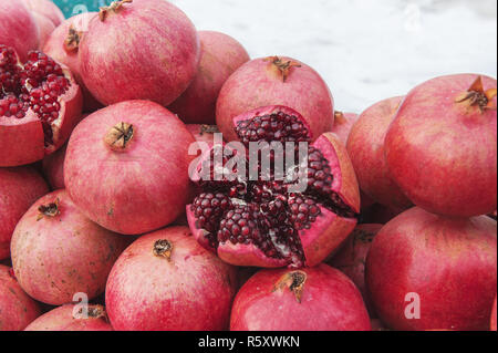 Ein Bündel von reifen roten Granatäpfel auf der Straße im Winter. Eine der Früchte halbiert. Sichtbare Körnung und Knochen. Close-up. Stockfoto