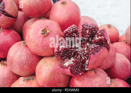 Ein Bündel von reifen roten Granatäpfel auf der Straße im Winter. Eine der Früchte halbiert. Sichtbare Körnung und Knochen. Close-up Stockfoto