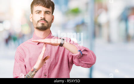 Jungen gutaussehenden Mann mit rosa Shirt über isolierte Hintergrund tun time out Geste mit den Händen, frustriert und ernstes Gesicht Stockfoto