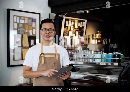 Portrait von asiatischen barista Holding digital Tablet am Zähler im Coffee Shop. Cafe Restaurant Service, Inhaber kleiner Unternehmen, die Lebensmittel- und Getränkeindustrie. Stockfoto