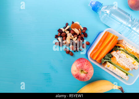 School Lunch Box mit Sandwich, Gemüse, Wasser, Nüssen und Früchten auf Türkisfarbenem Hintergrund. Gesunde Essgewohnheiten Konzept Stockfoto