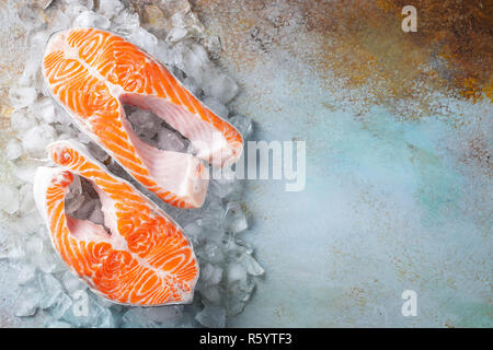 Zwei rohe frische Lachs oder Forelle Steaks auf Eis, die reich an Omega-3-Öl, mit Kalk, Thymian und Olivenöl auf einem blauen Hintergrund rostig. Gesunde und diätetische Lebensmittel. Stockfoto