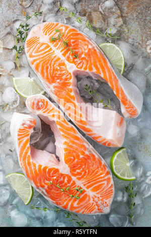 Zwei rohe frische Lachs oder Forelle Steaks auf Eis, die reich an Omega-3-Öl, mit Kalk, Thymian und Olivenöl auf einem blauen Hintergrund rostig. Gesunde und diätetische Lebensmittel. Stockfoto