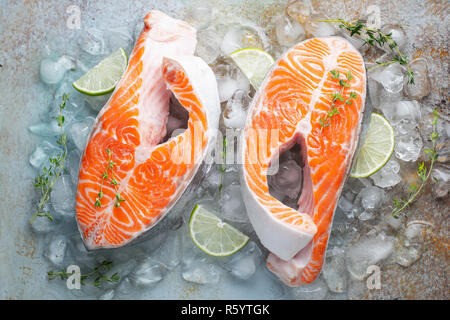 Zwei rohe frische Lachs oder Forelle Steaks auf Eis, die reich an Omega-3-Öl, mit Kalk, Thymian und Olivenöl auf einem blauen Hintergrund rostig. Gesunde und diätetische Lebensmittel. Stockfoto