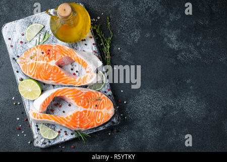 Zwei rohe frische Lachs oder Forelle Steaks, reich an Omega-3 Öl, mit Kalk, Thymian und Olivenöl auf einem dunklen Hintergrund. Gesunde und diätetische Lebensmittel. Ansicht von oben wit Stockfoto