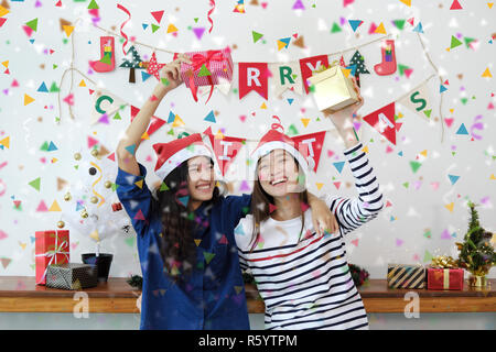 Zwei schöne Frauen in Santa Hüte und Holding Geschenkboxen Spaß mit bunten Konfetti an der Weihnachtsfeier. Stockfoto