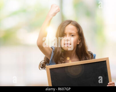 Brunette hispanic Girl holding Blackboard genervt und frustriert schrie mit Zorn, verrückt und schreien mit erhobener Hand, Wut Konzept Stockfoto