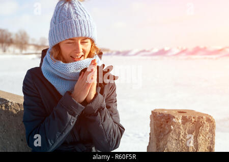 Das Konzept der livestyle Outdoor im Winter. Eine junge Frau in einem blauen Strick Hut und Mantel Lächeln, erwärmt sich und Spaziergänge durch den Winter Mou Stockfoto