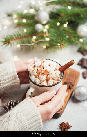 Holding Tasse heiße Schokolade mit Marshmallows und Zimt. Mädchen in Form gestrickter Pullover mit heißen Getränk. Selektive konzentrieren. Gemütliche Weihnachten Konzept Stockfoto