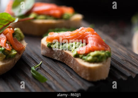 Toast mit Avocado und geräuchertem Lachs auf Holz serviert. Detailansicht, selektiver Fokus Stockfoto