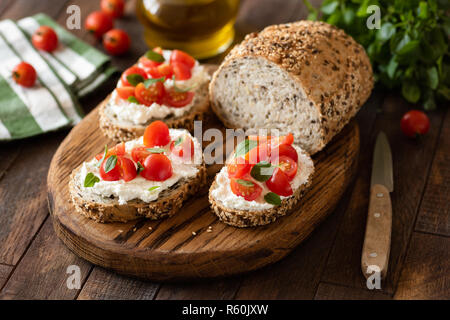 Bruschetta mit ricotta Käse und Kirschtomaten auf Vollkornbrot mit Samen. Auf hölzernen Schneidebrett serviert. Stockfoto