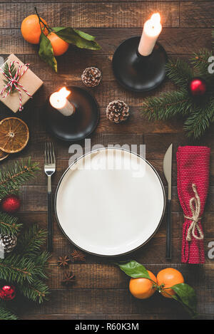 Rustikale Weihnachten Tisch mit Kerzen, leeren Teller, Besteck, Pine Tree Branches, Kegel und Mandarinen. Ansicht von oben Stockfoto