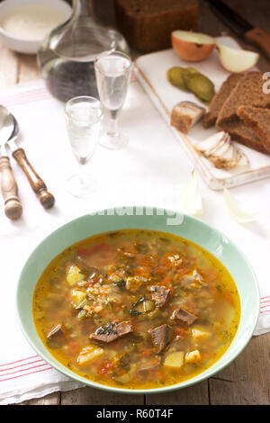 Rassolnik, traditionelle russische Suppe, serviert mit verschiedenen Snacks und Wodka. Im rustikalen Stil. Stockfoto