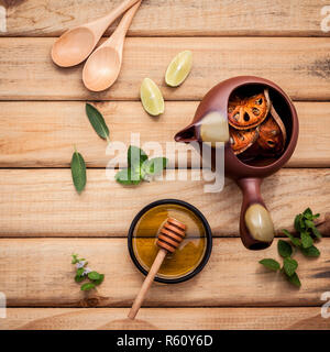 Kräutertee Topf mit frischen Kräutern Salbei, Pfefferminze, getrocknete indischen bael, Honig und Limone Slice auf rustikalen Holzmöbeln Hintergrund. Stockfoto