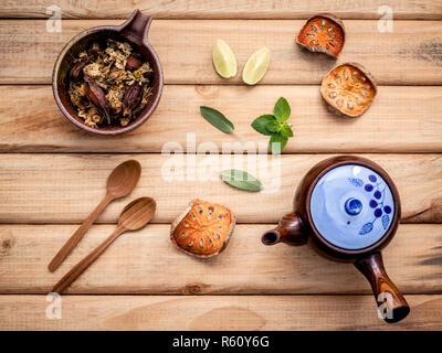 Kräutertee Topf mit frischen Kräutern Salbei, Pfefferminze, getrocknete indischen bael, getrocknete Chrysanthemen und Kalk Slice auf rustikalen Holzmöbeln Hintergrund. Stockfoto