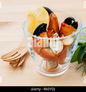 Frische gedämpfte Rote Krabben Bein in Glasschale. Rote Krabben Bein mit Zutaten. Gedämpfte Rote Krabben Bein mit Kräutern, Fenchel, Petersilie, Rosmarin, Zitrone und Minze mit Gabel auf bewaldeten Hintergrund. Stockfoto