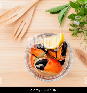 Frische gedämpfte Rote Krabben Bein in Glasschale. Rote Krabben Bein mit Zutaten. Gedämpfte Rote Krabben Bein mit Kräutern, Fenchel, Petersilie, Rosmarin, Zitrone und Minze mit Gabel auf bewaldeten Hintergrund. Stockfoto