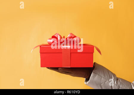 Close-up Teilansicht der Mann mit roter Geschenkbox auf gelben Hintergrund. Geschenk, das Konzept Stockfoto