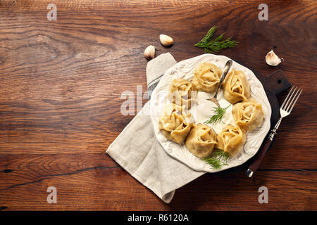 Asiatische gedünstete Teigtaschen Manti mit Dill und Knoblauch auf Holz- Hintergrund. Stockfoto