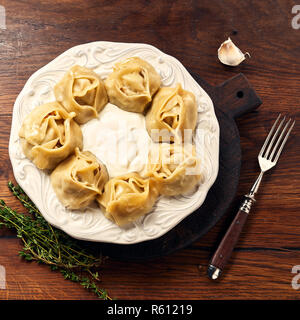 Asiatische gedünstete Teigtaschen Manti mit Dill und Knoblauch auf Holz- Hintergrund. Stockfoto